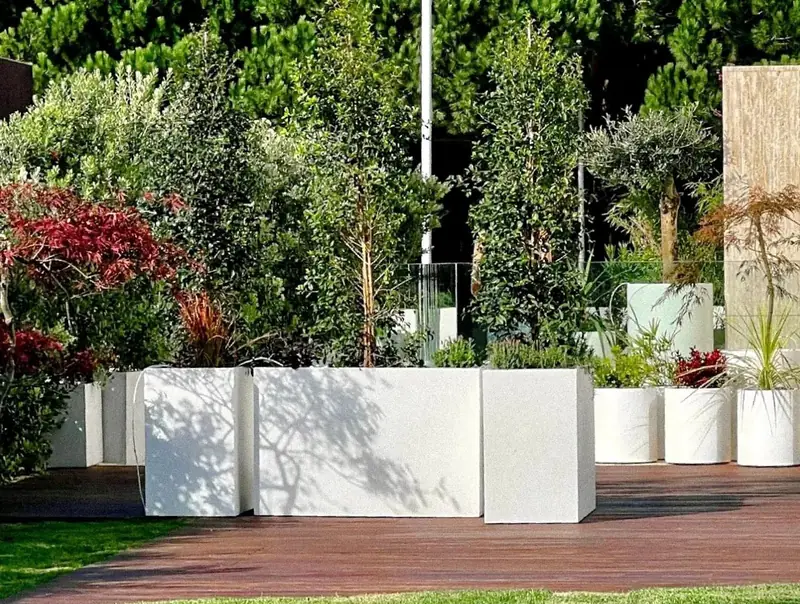 Rendered and lacquered planters of different heights, filled with grasses and flowering perennials beside a lawn.