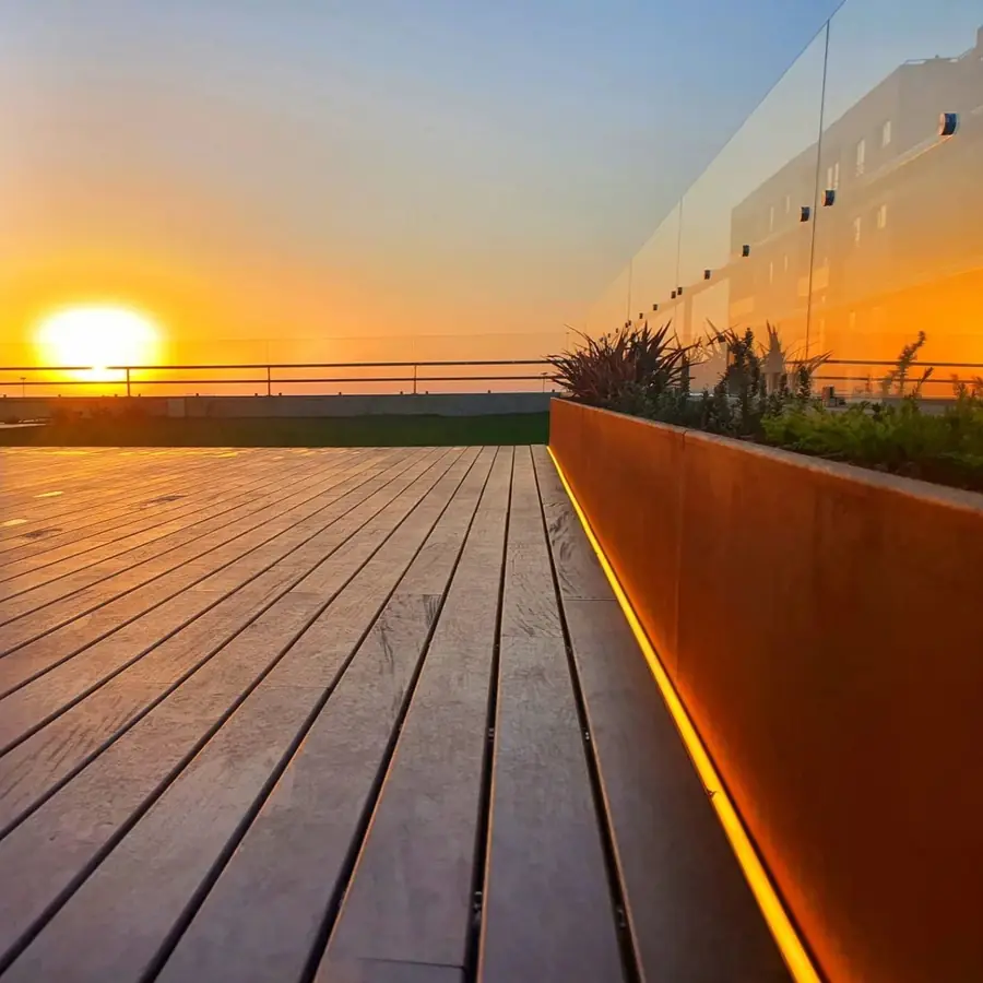 A hardwood roof deck at sunset with a Corten steel planter running the length of the glass balustrade.