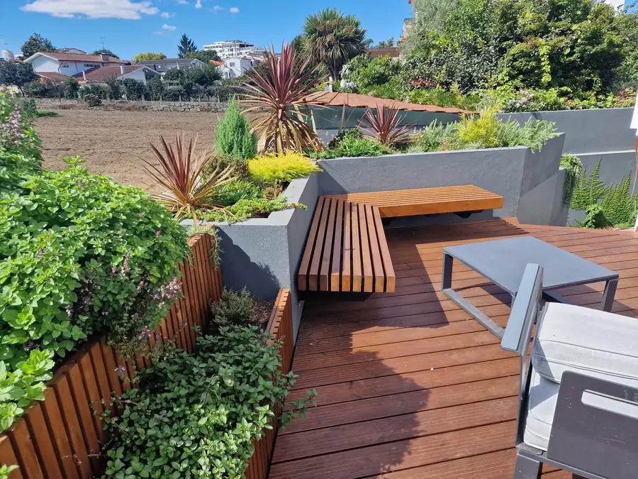 A roof terrace with a hardwood deck, a built-in timber bench and rendered planters full of grasses and palms.